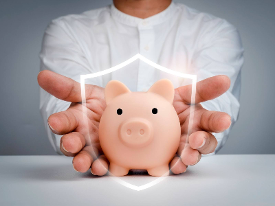 Un par de manos abiertas sostienen y protegen una alcancía con forma de cerdito, la cual está rodeada por el contorno brillante de un escudo digital