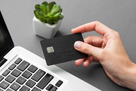 Una mano sostiene una tarjeta de crédito negra frente a una computadora portátil, sugiriendo el inicio de una compra o transacción digital.