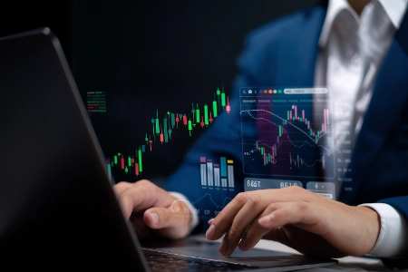 muestra a una persona de negocios trabajando en una computadora portátil, con una interfaz digital superpuesta que proyecta gráficos de velas financieras y análisis de mercado en 3D.