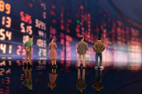 Cuatro figuras en miniatura observan de espaldas un gran panel digital repleto de números e información bursátil.
