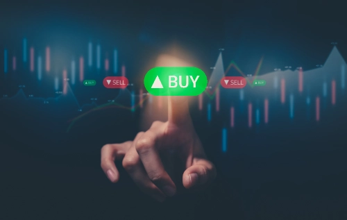 Un dedo presiona un botón verde flotante que dice "BUY" frente a un gráfico bursátil digital de trading.