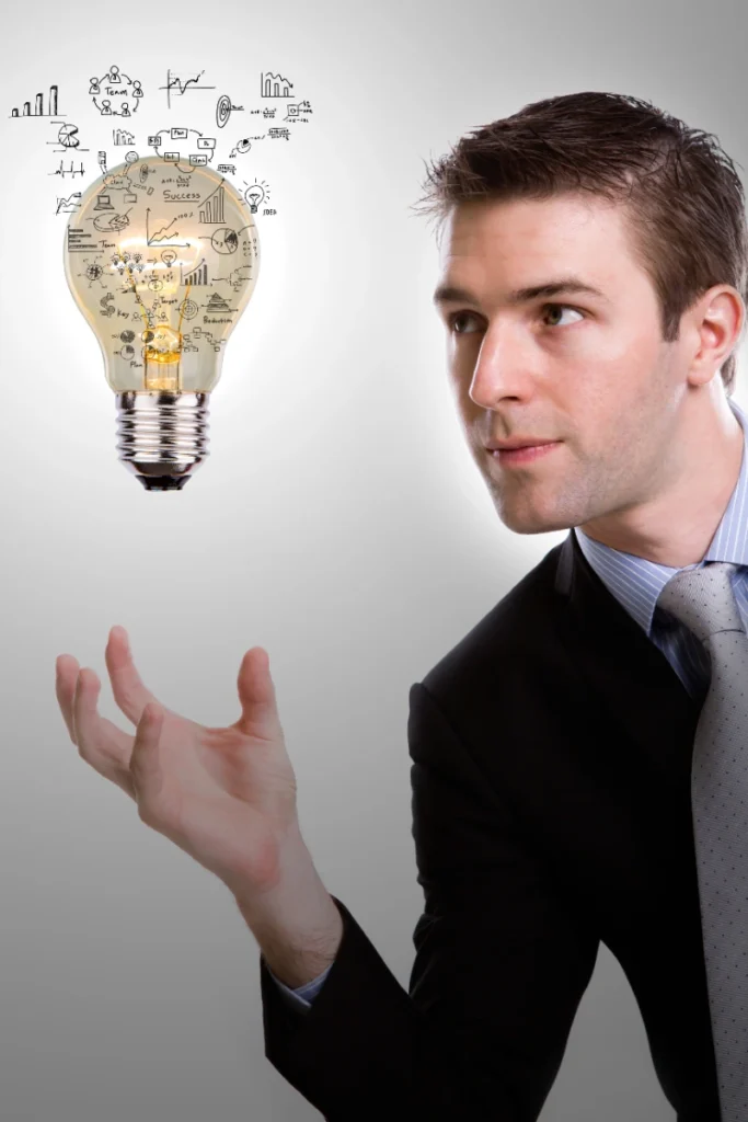Empresario observando detenidamente una bombilla encendida que flota sobre su mano, de la cual emanan esquemas y diagramas de estrategia empresarial.
