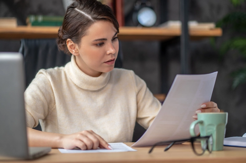 Profesional concentrada revisando documentos impresos en su escritorio de trabajo, representando la auditoría de procesos, el análisis de contratos y la gestión corporativa.