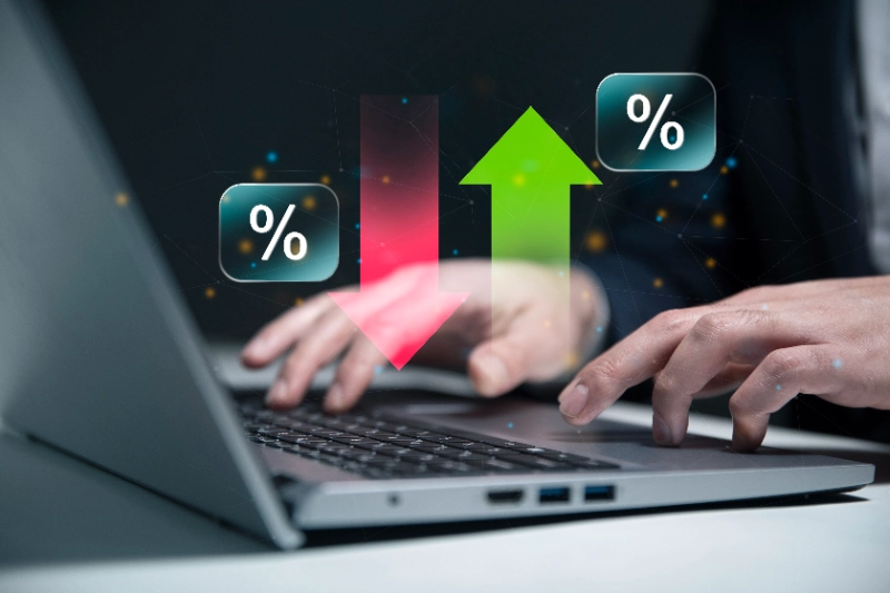 Usuario operando una laptop con superposición gráfica de porcentajes y flechas de tendencia, representando tasas de interés y volatilidad del mercado.